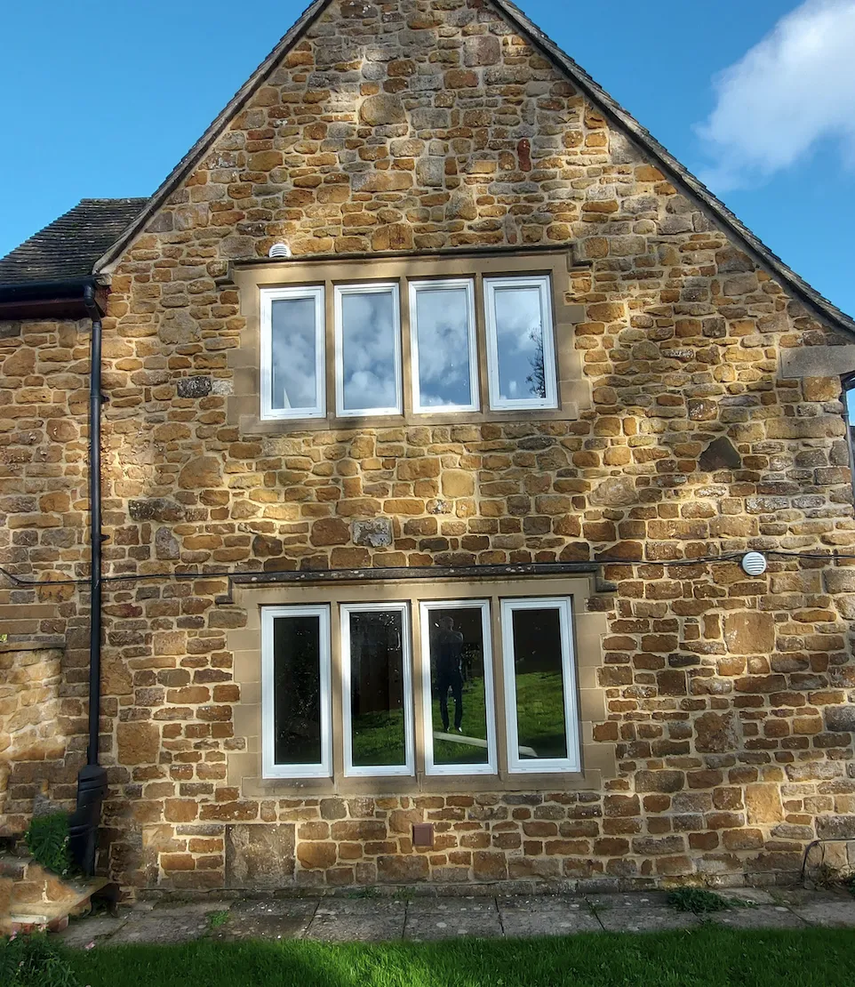 The rear stone elevation of Orchard House after the works, new white-framed windows sitting in the dressed stone mullions