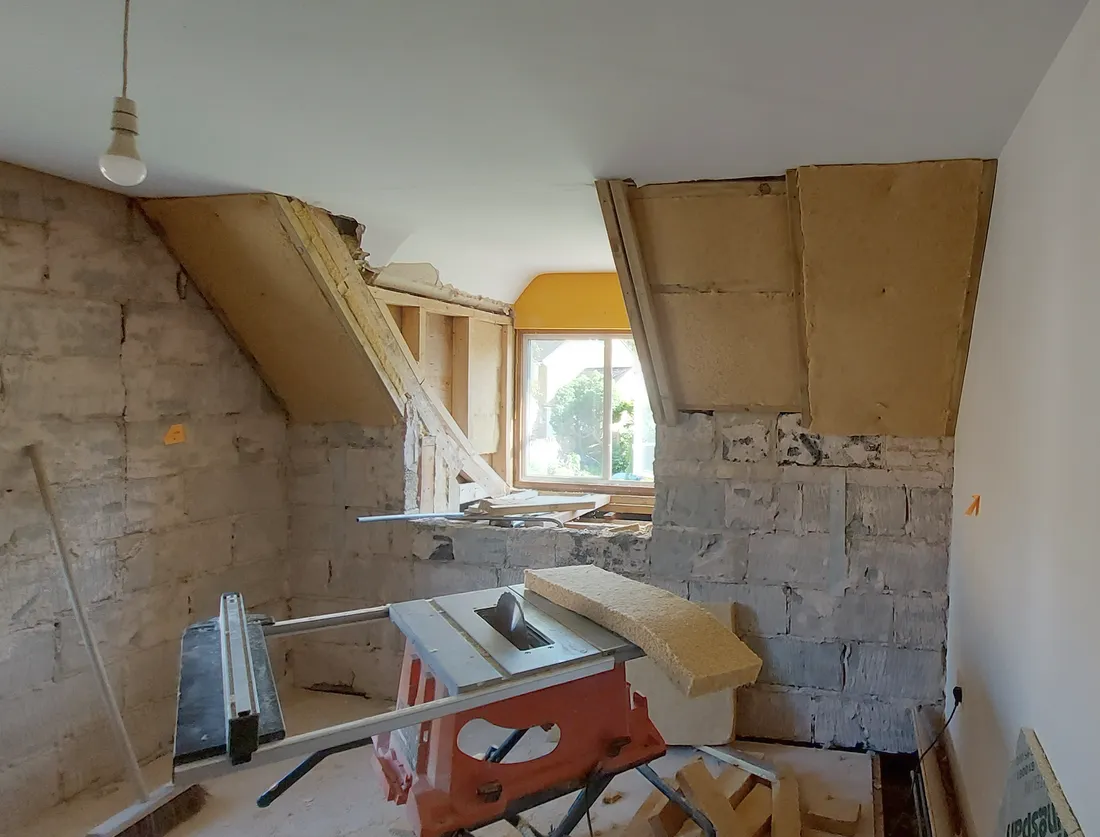 Wood fibre boards fitted to the opened sloping ceilings of a bedroom, with a saw bench set up mid-room
