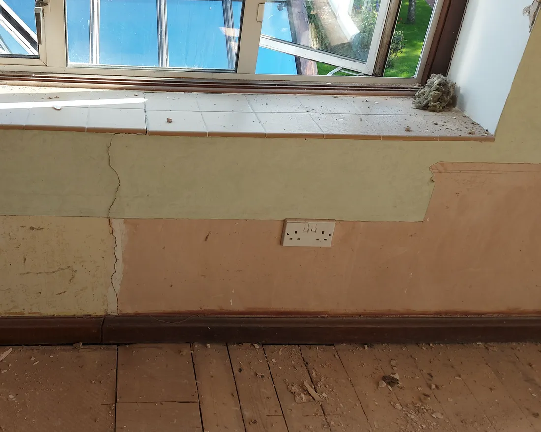 A window wall mid-strip-out, old tiled cill and failed plaster being removed back to sound masonry