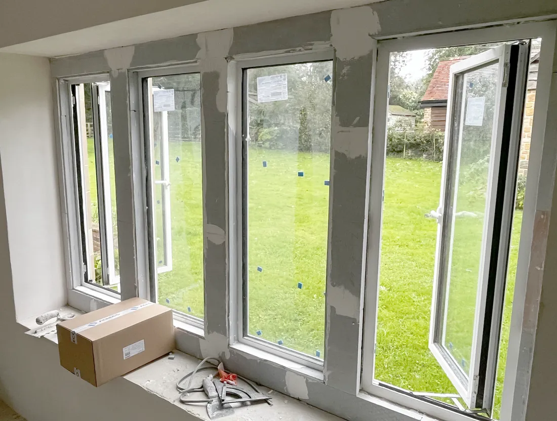 New white-framed windows fitted within the stone mullions, seen from inside with protective labels still on