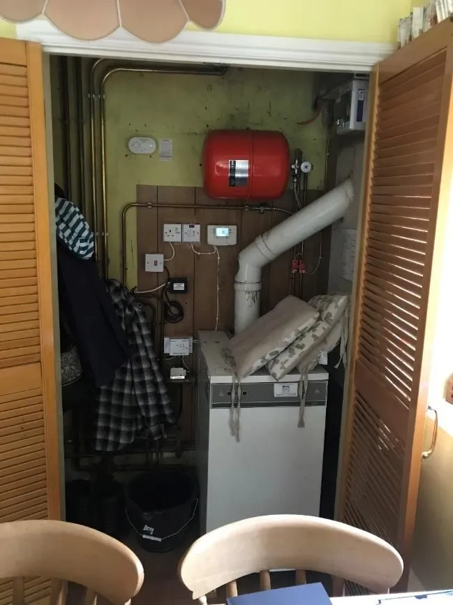 Outgoing oil boiler in a kitchen cupboard with flue and expansion vessel above